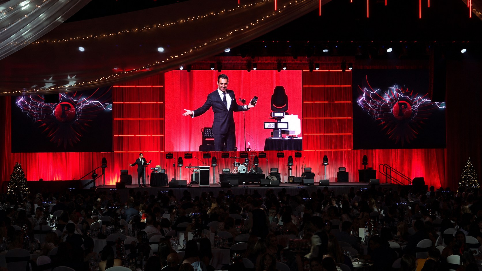Phoenix on a red-lit gala stage, live on the big screen above a packed room of round tables